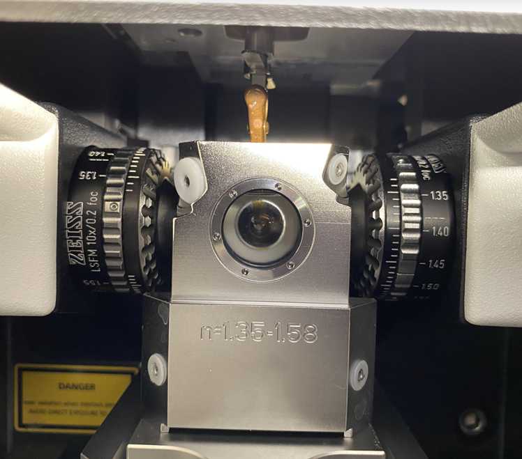 Fig. 12: How the sample should be mounted prior to imaging (20x). The sample should be directly facing the detection objective and perpendicular to the dual illumination objectives. The glass cover slip should be facing towards the front port window. 5x mounting will look similar, but with its respective chamber and lenses. Fig. 12: How the sample should be mounted prior to imaging (20x). The sample should be directly facing the detection objective and perpendicular to the dual illumination objectives. The glass cover slip should be facing towards the front port window. 5x mounting will look similar, but with its respective chamber and lenses.